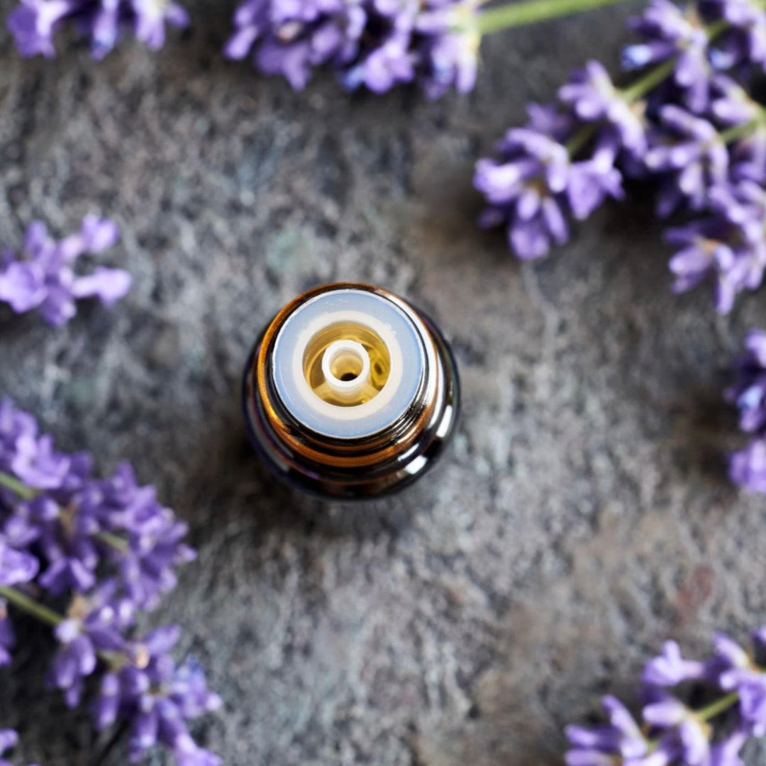 Essential oil bottle cap surrounded by lavender flowers on a stone surface