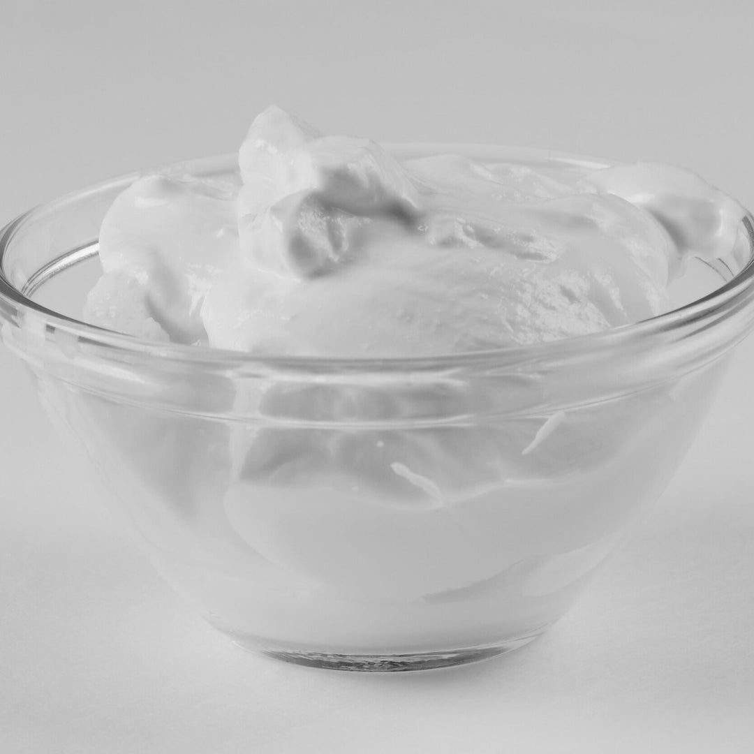 Glass bowl filled with white cream on a light gray background